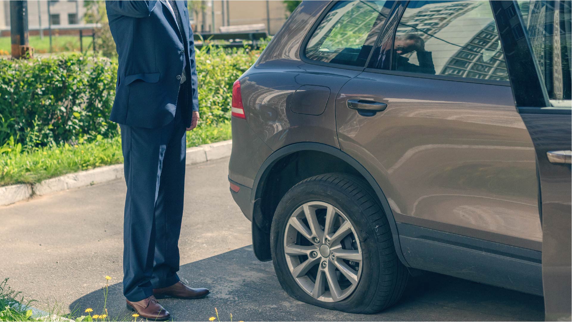 Un homme se tient près de sa voiture qui a un pneu crevé