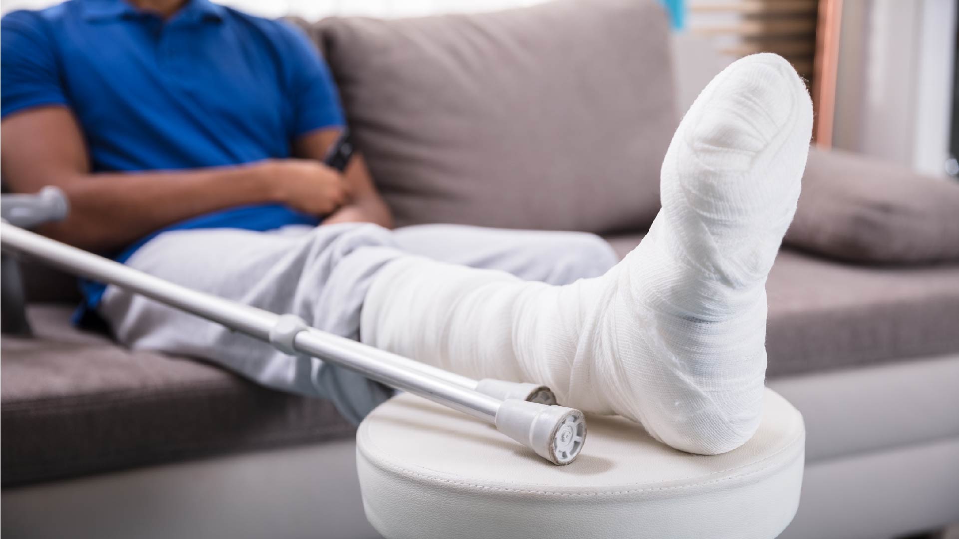 Un monsieur est assis dans son canapé avec le pied plâtré posé sur un tabouret