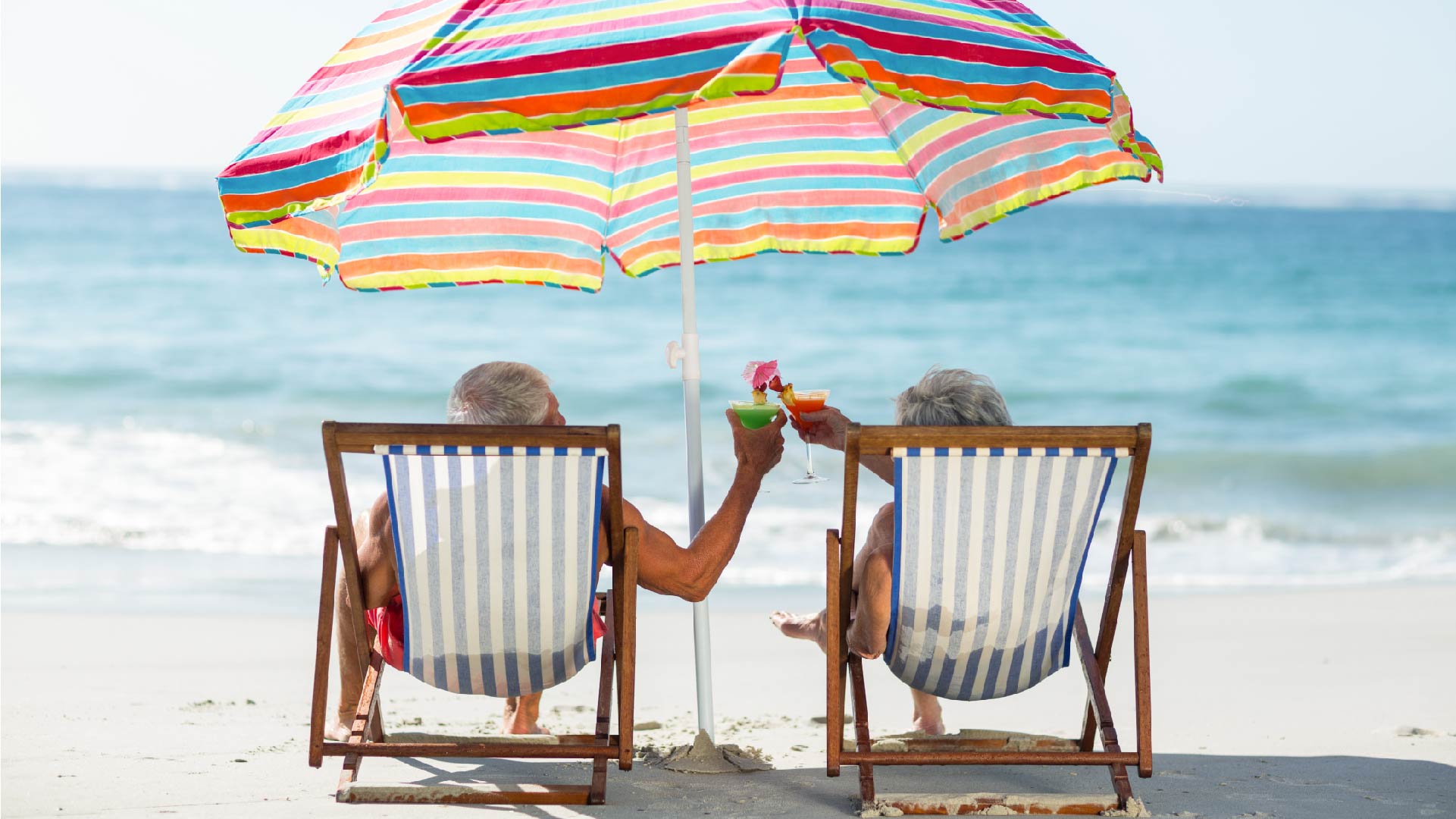 Een koppel oudere mensen drinkt een cocktail op het strand