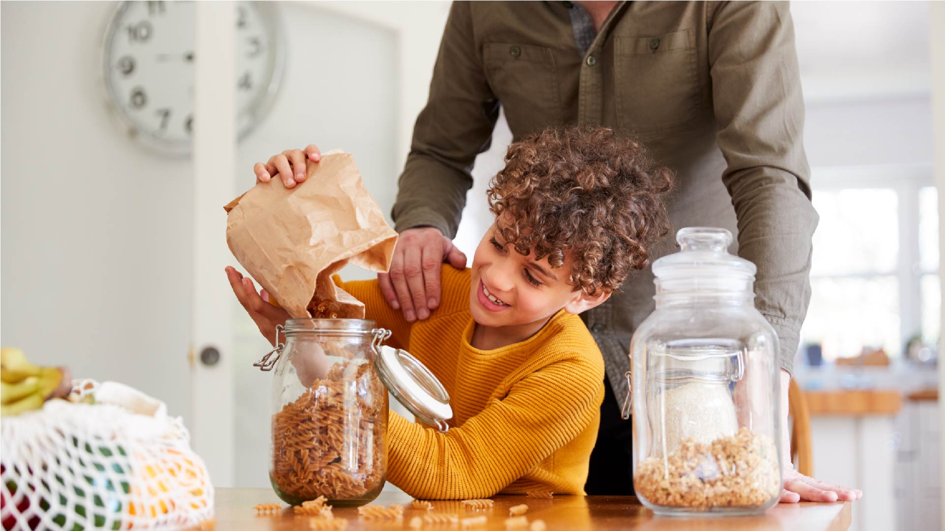 Een jongen helpt zijn papa in de keuken om glazen bokalen te vullen met eten