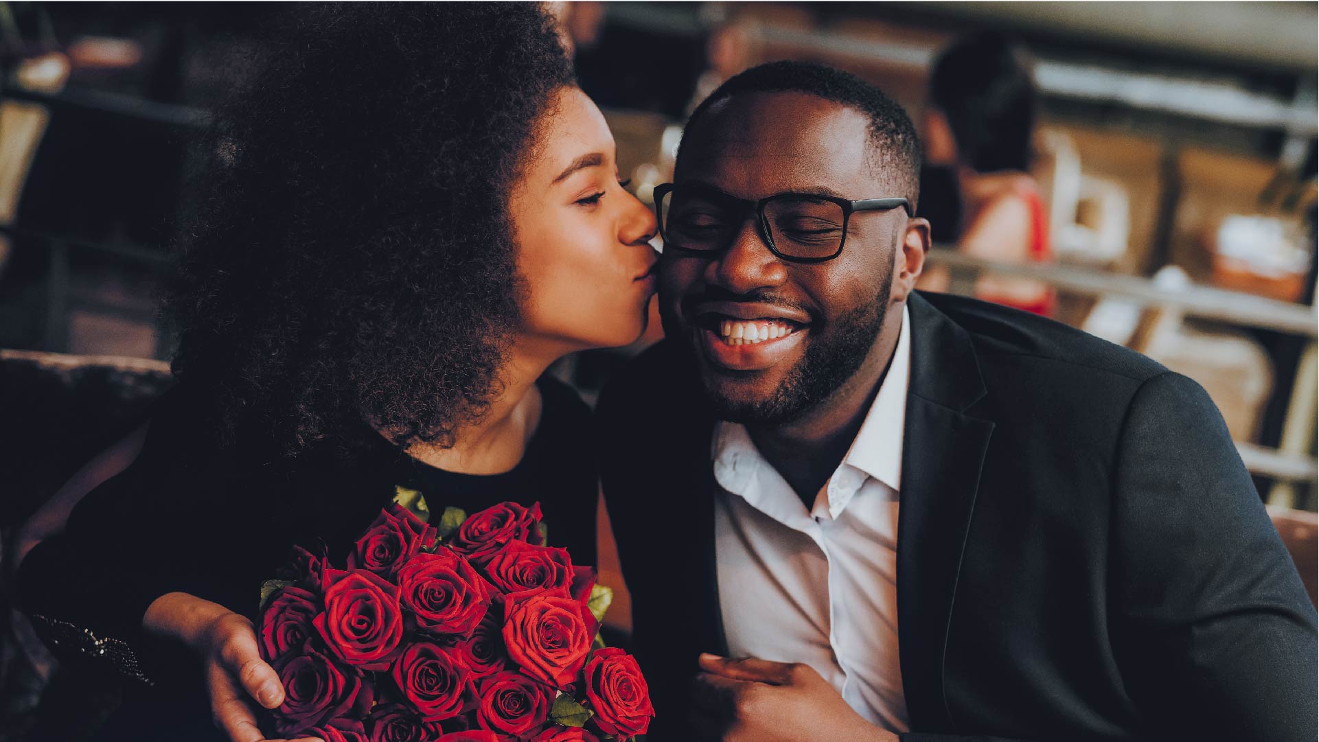 Een koppel waarbij de vrouw haar man kust om hem te bedanken voor het boeket rode rozen