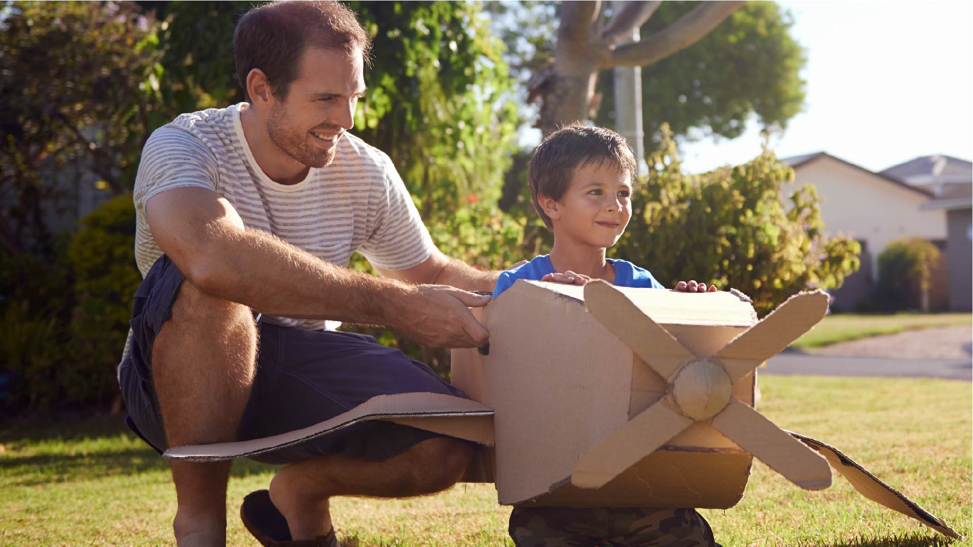 Een vader en een zoon spelen in de tuin met een kartonnen vliegtuigje