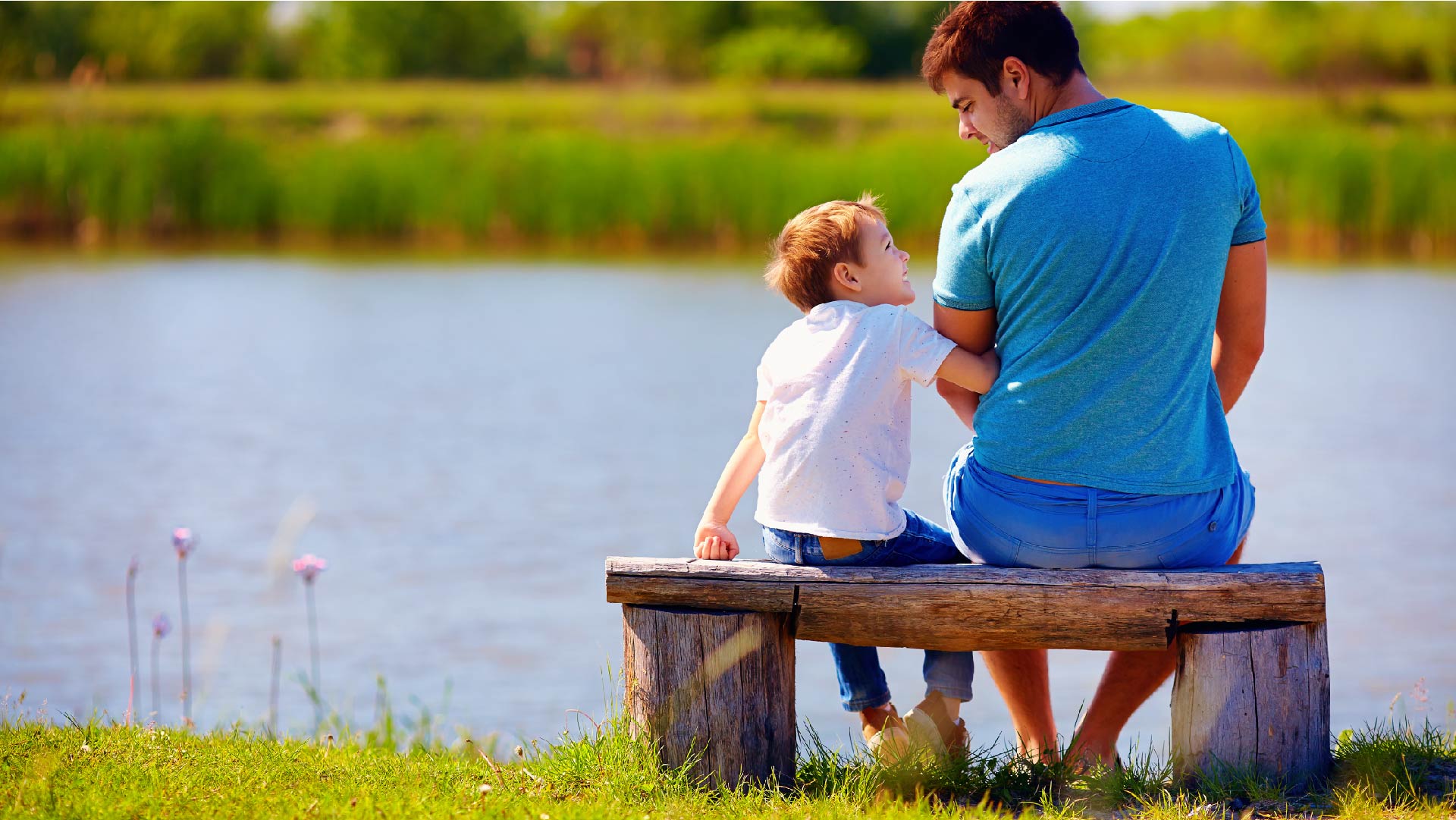 Een vader en een zoon zitten op een bankje aan een rivier