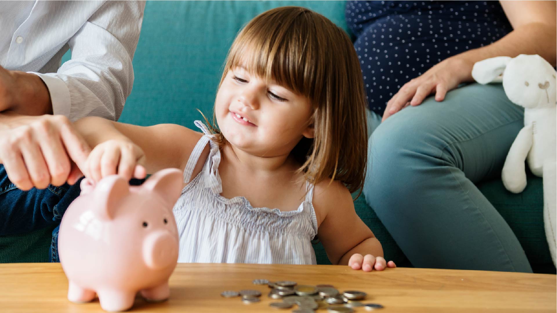 Vergezeld van haar ouders, steekt een meisje muntstukken in een spaarpot