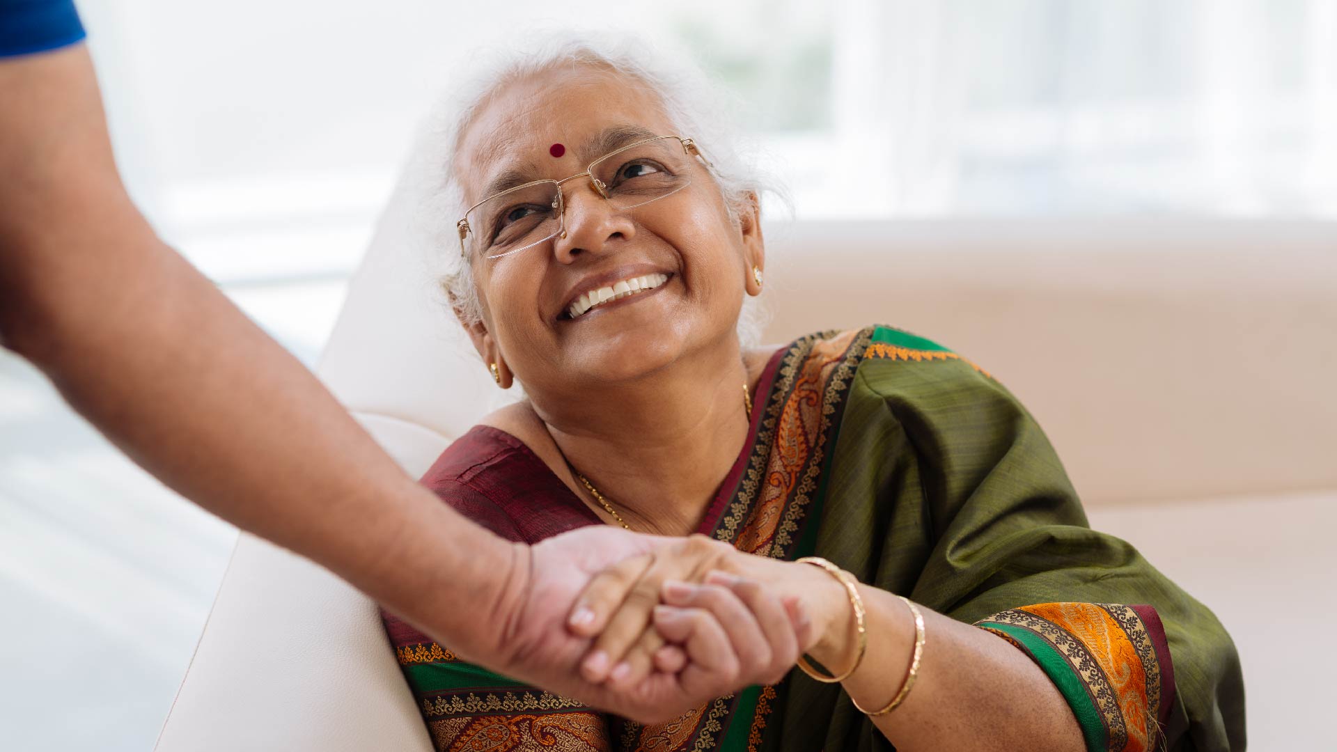 Une dame âgée tient une main tout en souriant à la personne