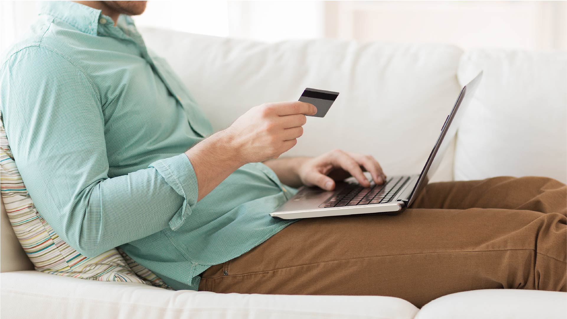 Un homme couché dans le canapé fait des paiements avec sa carte et son ordinateur