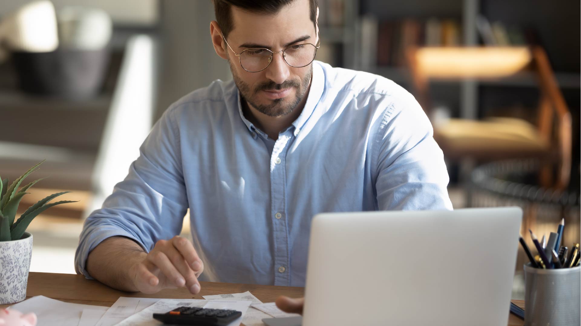 Een man werkt op zijn computer en gebruikt zijn rekenmachine