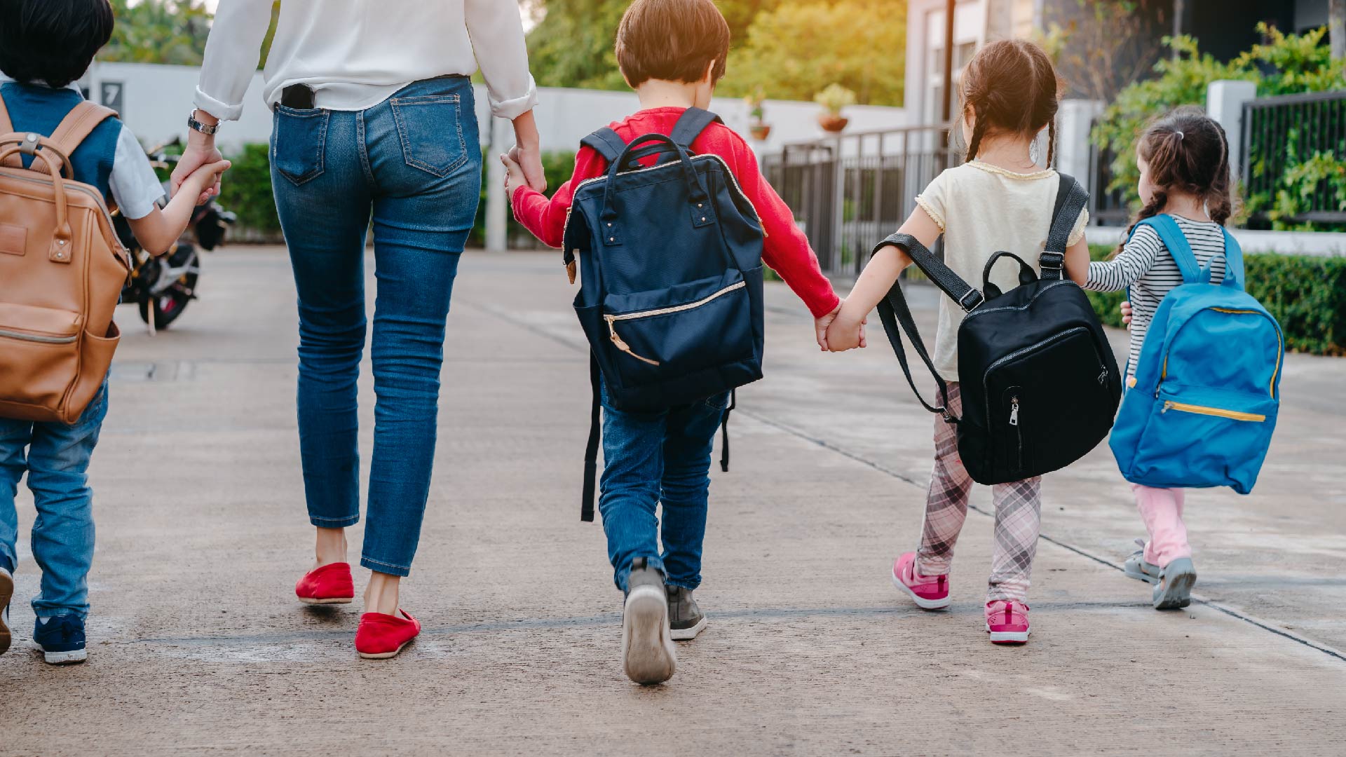 Een mama brengt haar vier kinderen naar school en geeft hen een hand