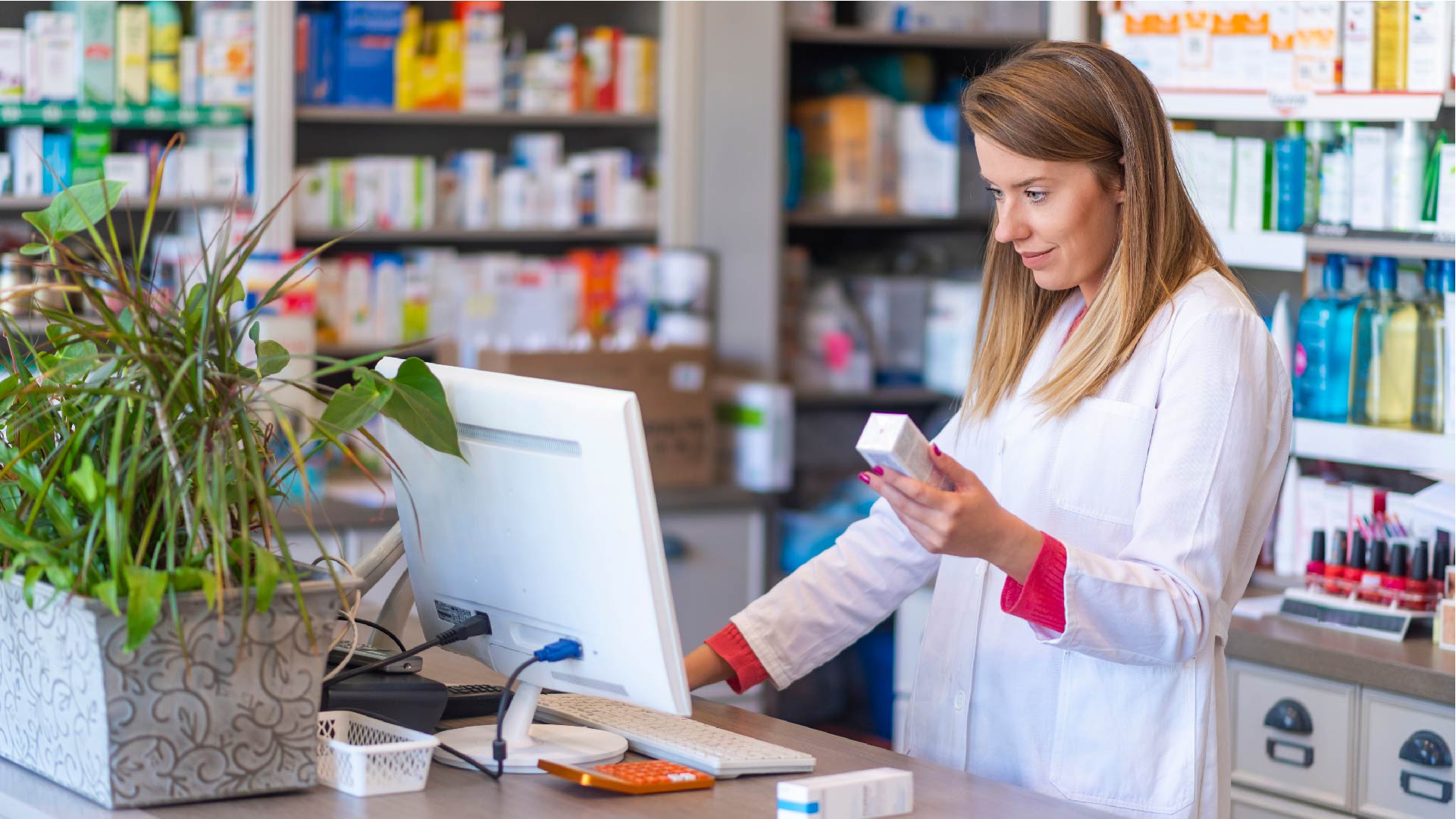 Une pharmacienne tient une boite de médicaments et regarde son ordinateur