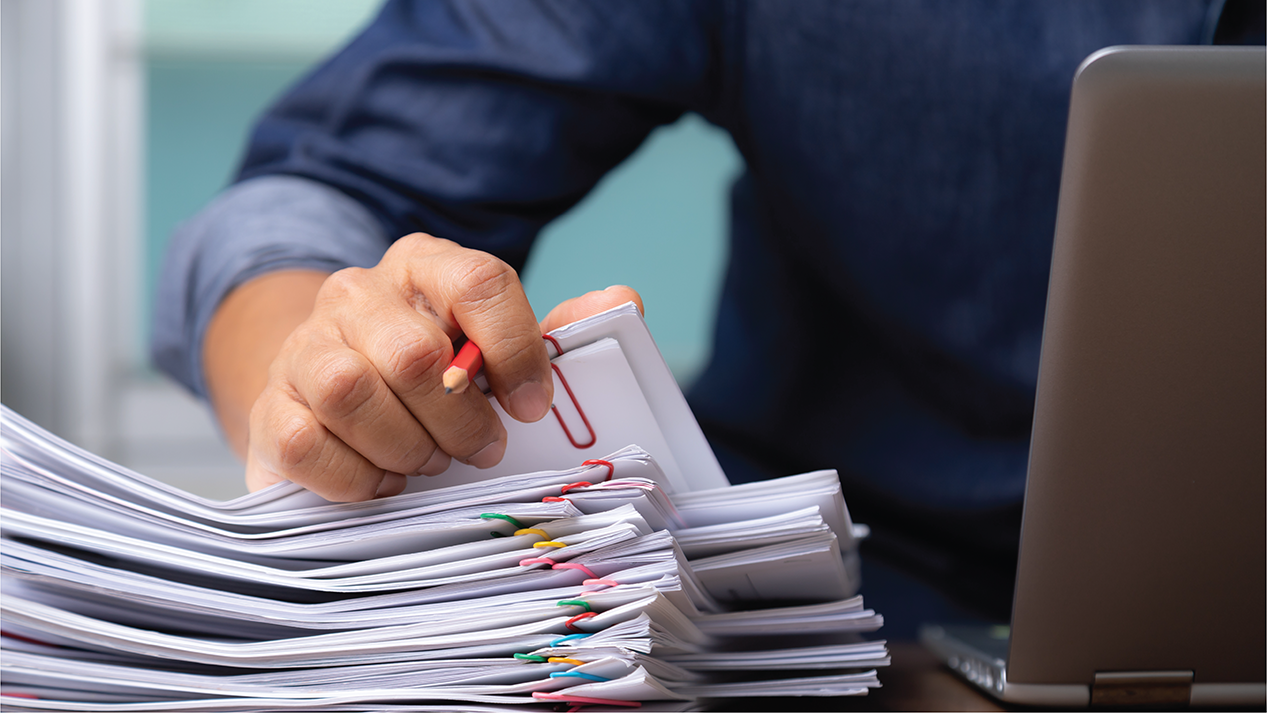 Un homme a une pile des documents dans ses mains à coté son laptop Un homme a une pile des documents dans ses mains à coté son laptop