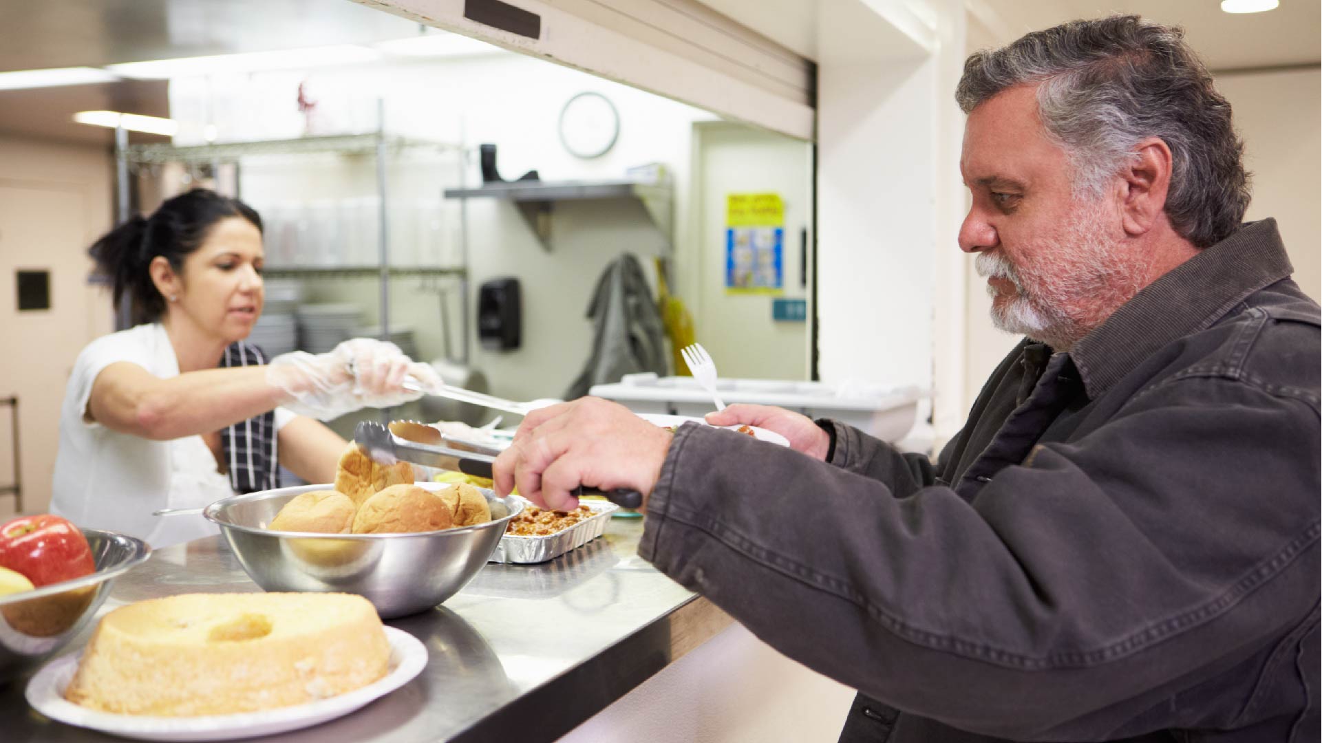 Une cuisinière bénévole sert un repas à un homme sans-abris