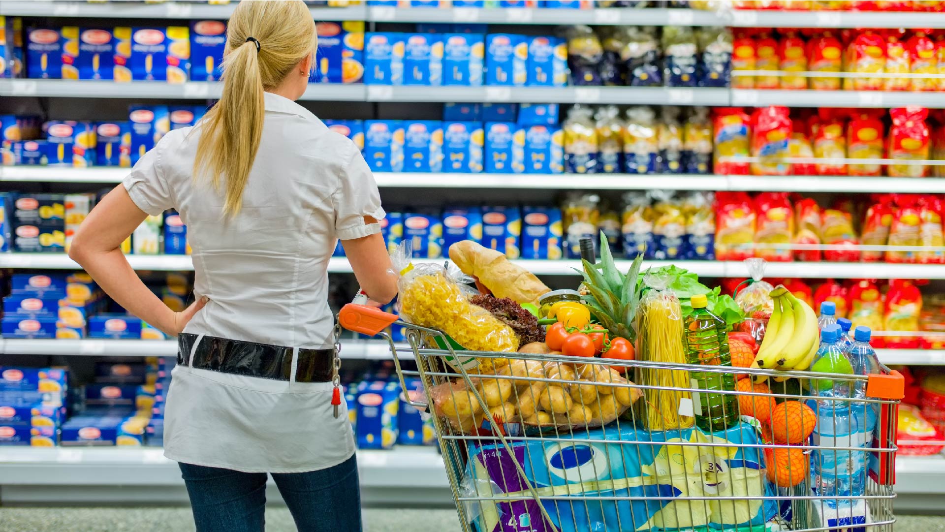 Une femme compare les marques de pâtes dans le rayon du supermarché