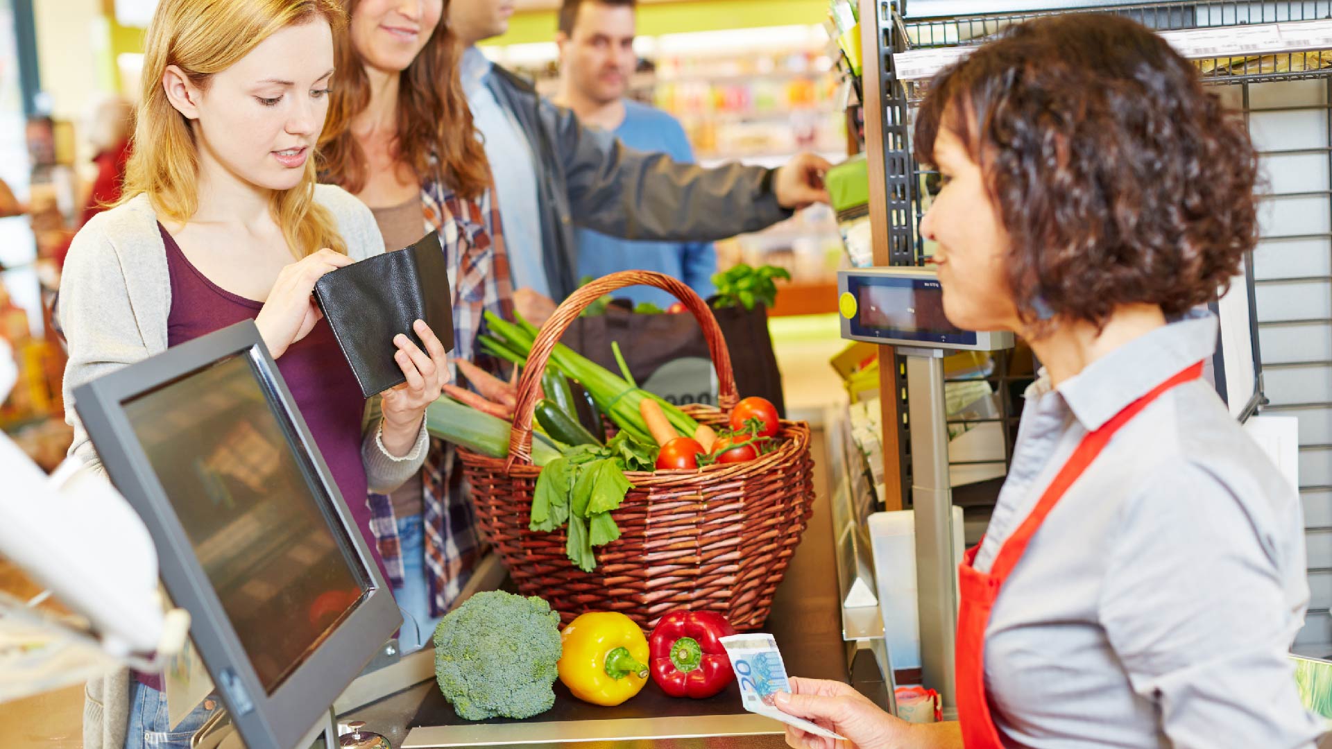 Une jeune femme à la caisse d&#039;un supermarché sort son porte-feuille pour payer