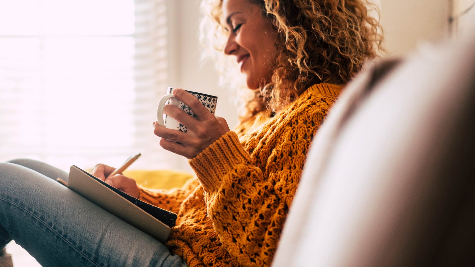 Een vrouw schrijft in haar notaboekje terwijl ze koffie drinkt