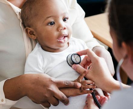 Een baby zit op de schoot van zijn mama tijdens een onderzoek bij de kinderarts