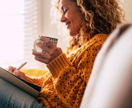 Un femme écrit dans son carnet en buvant un café