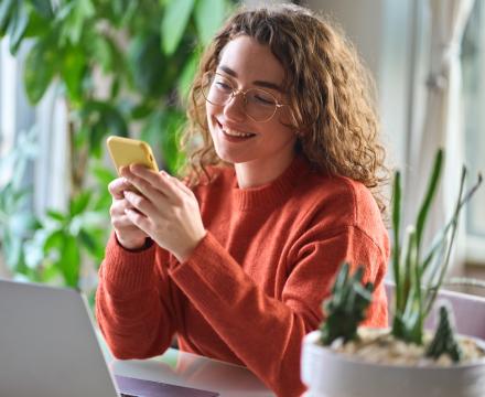 Une jeune femme sourit en regardant son smartphone